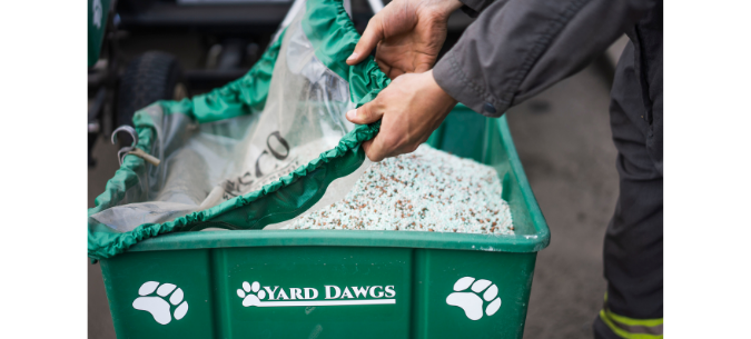 lawn care technician pulls cover over fertilizer spreader filled with granules of fertilizer