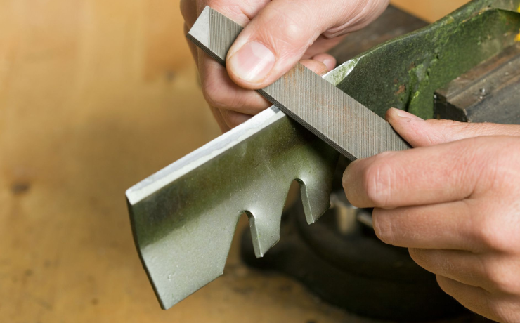 man sharpens a mower blade with a file