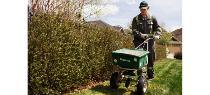 lawn care technician uses a spreader to apply fertilizer to a lawn